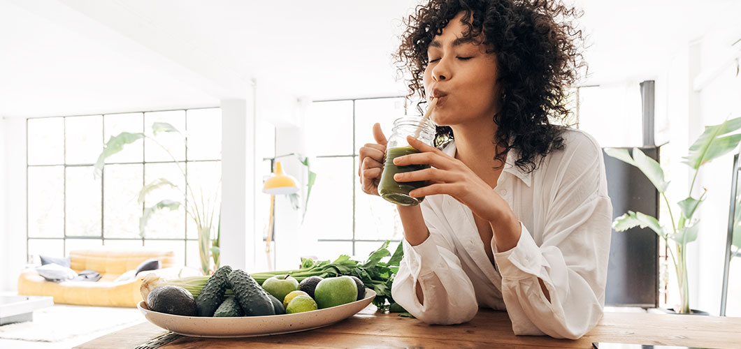 Jovem mulher bebe um smoothie verde com CBD.